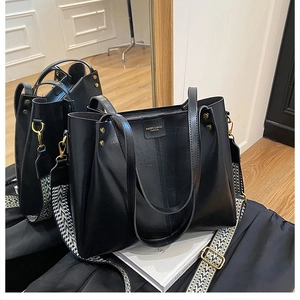 Detail view of large black tote bag with wide geometric strap and embossed fashion logo