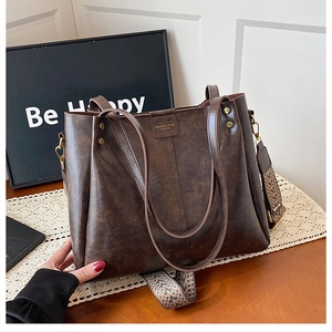 Close-up of vintage brown leather tote bag with a patterned woven shoulder strap
