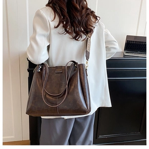 Detail of dark brown tote bag featuring embossed logo and woven geometric shoulder strap