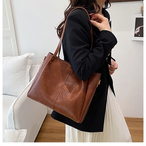 Detailed side view of large caramel brown tote bag worn by a model in black blazer