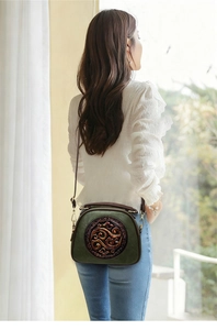 Detail of dark green crossbody bag with vintage embossed patterns and metal zip