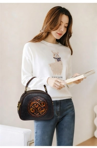 Close-up of a black leather handbag with a traditional orange embossed circular pattern