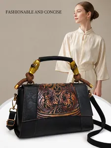 Detailed view of black leather ethnic handbag featuring carved floral patterns and bamboo handle