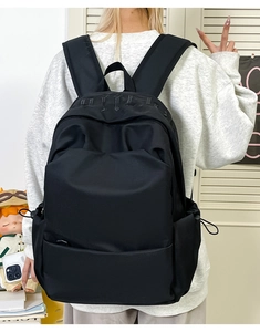 Rear view of a black minimalist backpack featuring an embossed logo and side drawstring pockets