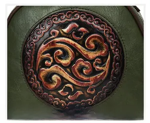 Macro view of dark green leather shoulder bag with embossed floral scroll patterns