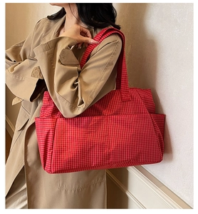 Detail view of large red plaid tote bag with wide strap on a model wearing a beige trench coat
