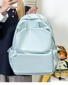 Detail of light blue nylon backpack with embroidered letters and multi-pocket design