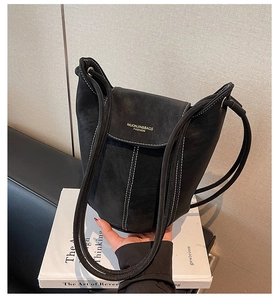 Detail of black bucket bag featuring white contrast stitching and gold lettering on the flap