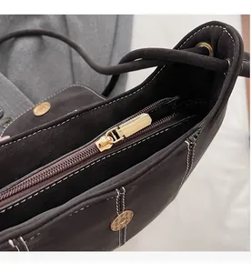 Close-up of smooth gold metal zipper and white contrast stitching on brown suede bucket bag