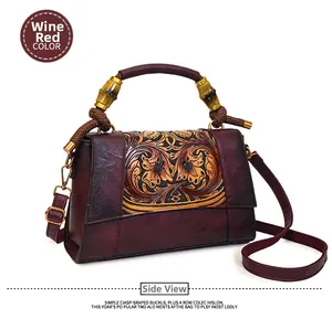 Detail of vintage burgundy leather handbag featuring floral embossing and bamboo handle