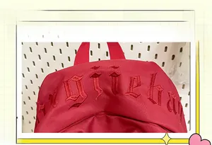 Close-up of red canvas backpack featuring 3D gothic embroidery and durable webbing handle