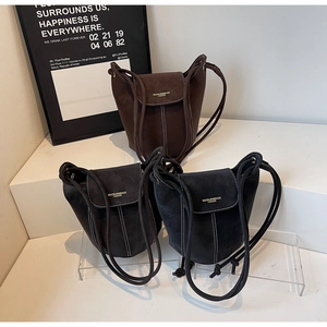 Detail of suede bucket bags in brown, grey, and black with contrast stitching and gold logo