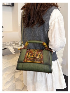 Detailed view of a green leather handbag with floral carving and bamboo handle on model