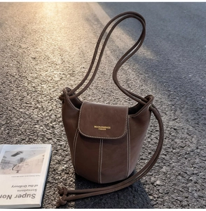 Detailed view of a brown suede bucket bag with white contrast stitching and shoulder strap