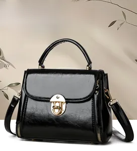 Close-up of black glossy leather handbag featuring golden metal buckle and side zipper