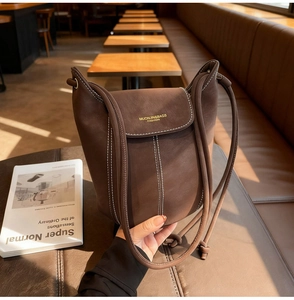 Detailed view of dark brown bucket bag with contrast stitching and golden logo on side