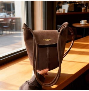 Close-up of brown suede bucket bag with white contrast stitching and gold logo
