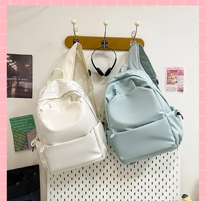 Detail view of cream and light blue nylon backpacks with relief letter decoration
