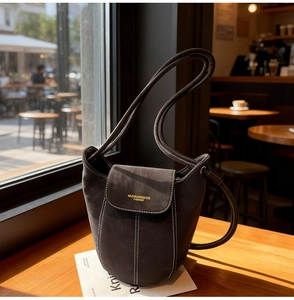 Detail of suede bucket bag featuring contrast white stitching and gold logo lettering