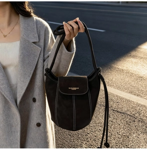 Detail of dark brown suede bucket bag featuring contrast stitching and gold logo