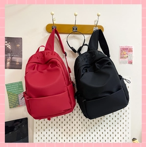Detail view of red and black canvas backpacks with Gothic letter embroidery on a wall