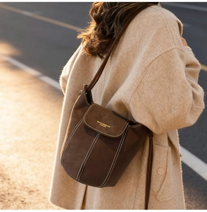 Close-up of brown suede bucket bag with contrast stitching and gold logo detail