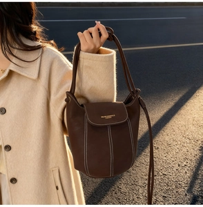 Detailed view of a brown suede bucket bag featuring white stitching and gold lettering