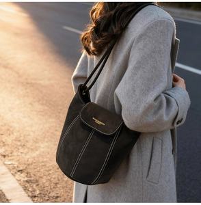 Detail view of black suede bucket bag featuring contrast white stitching and gold logo