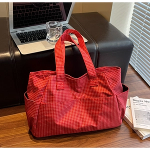Detail of red checkered canvas tote bag with side pockets on a dark wooden floor