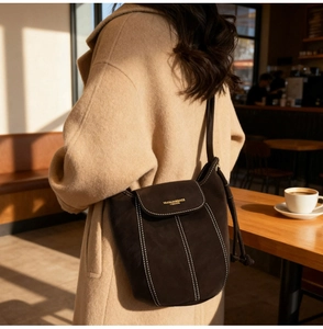 Detail of dark brown suede bucket bag with contrast stitching on a beige wool coat