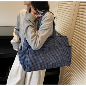 Model wearing a large navy blue plaid tote bag with side pockets and canvas texture