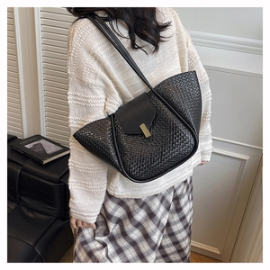 Detailed view of black woven tote bag with golden buckle and leather shoulder strap