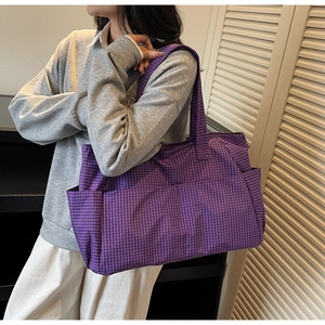 Close-up of a large purple checkered tote bag with side pockets shown on a model's shoulder
