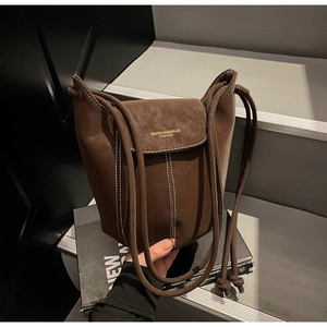 Detail of a brown suede bucket bag featuring contrast white stitching and gold logo print