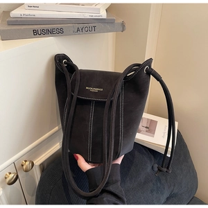 Close-up of black suede bucket bag with white contrast stitching and shoulder strap details