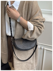 Close-up of black crescent crossbody bag with silver rivet studs on adjustable strap