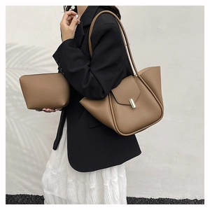Detail of dark brown leather tote bag with gold metal clasp on model in black blazer