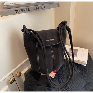 Detail of suede bucket bag featuring contrast white stitching and minimalist shoulder strap