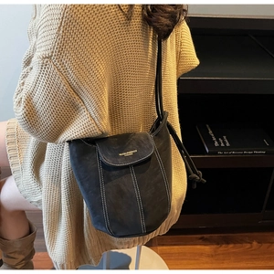 Close-up of black suede bucket bag with white contrast stitching worn by a model