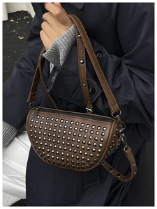 Detailed close-up of brown leather half-moon bag with decorative silver metal studs