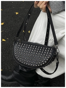 Close-up of a black half-moon shoulder bag with silver studs on a street background