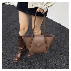 Brown woven textured tote bag with gold buckle fastener shown in a lifestyle street shot