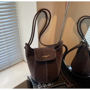 Detail of dark brown faux suede bucket bag with contrast stitching and branded flap closure