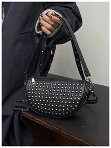 Close-up of black leather crescent bag with silver rivet studs and top zipper detail
