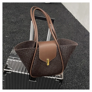 Detail of woven texture brown tote bag with gold metal buckle on silver suitcase