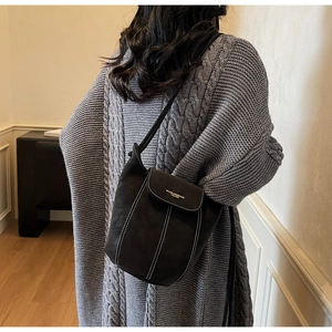 Detail of black suede bucket bag with white contrast stitching and logo on knit cardigan