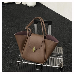 Close-up of brown litchi leather handbag with golden metal twist lock on a suitcase