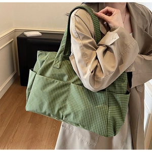 Detail of green checkered canvas tote bag showing multiple external storage pockets