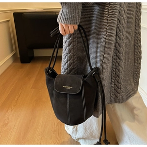 Detail of matte black suede bucket bag with white stitching and drawstring strap