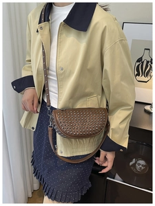 Brown leather crescent bag with silver stud accents shown on a model in a trendy outfit